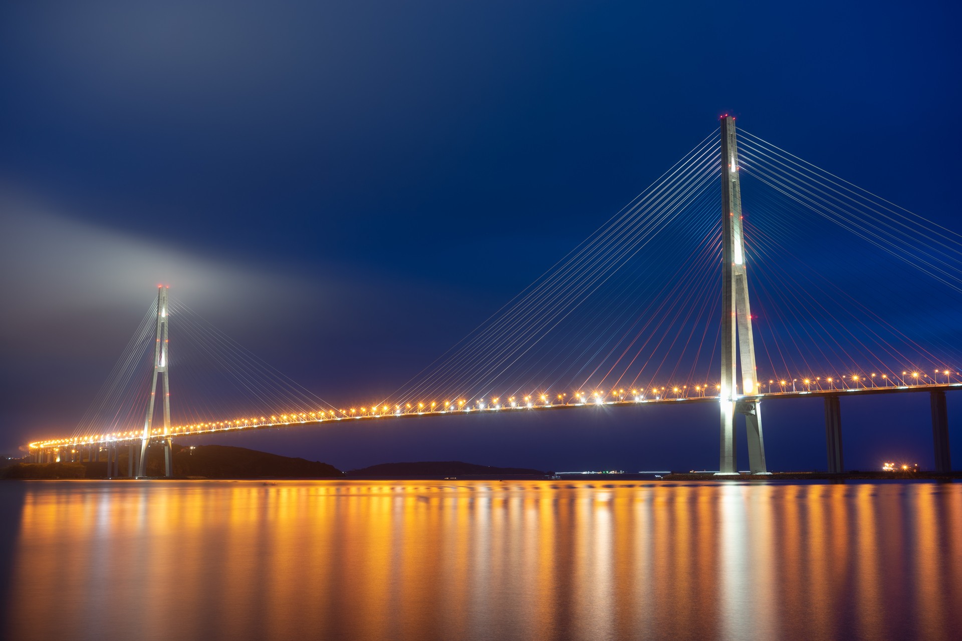 Ночной пейзаж Владивостока. Русский мост на фоне моря.